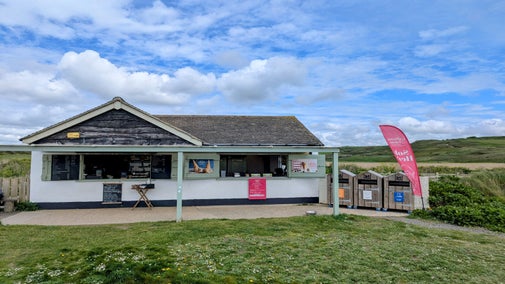 A small building with a veranda and two shuttered windows open, with signs and a table in front.